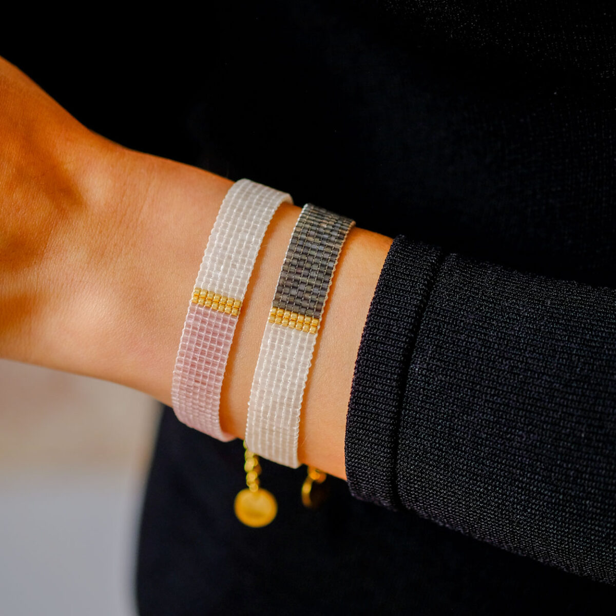 Close-up view of beaded bracelets in various designs worn on a woman's wrist against a dark sleeve.