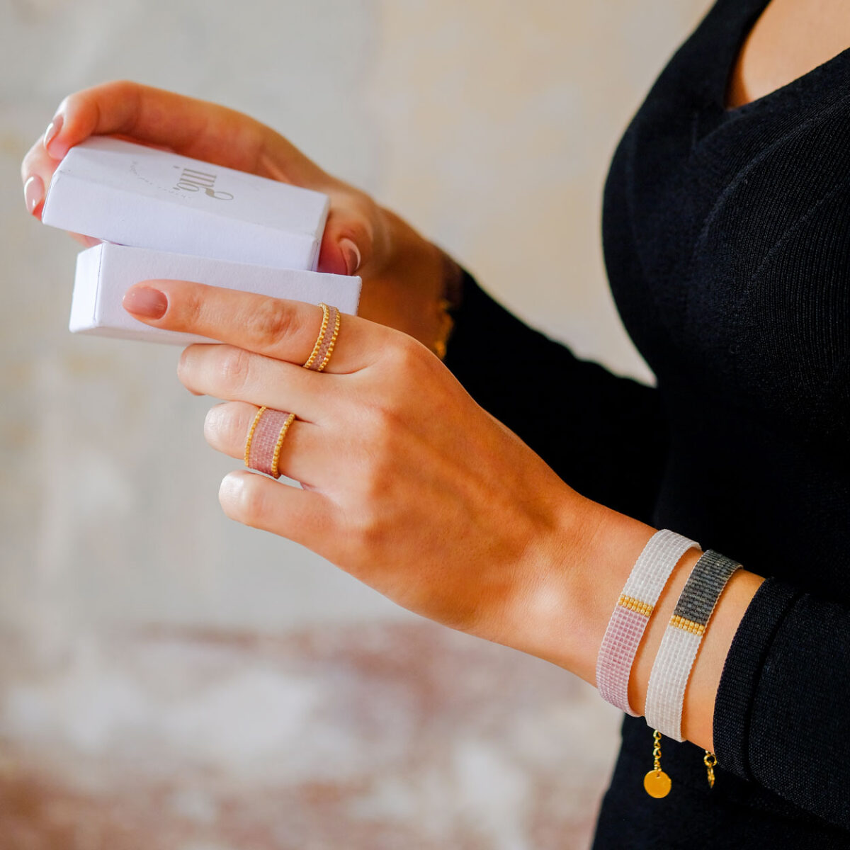 Close-up of a woman's hands holding a white jewelry box with elegant bracelets and golden rings.