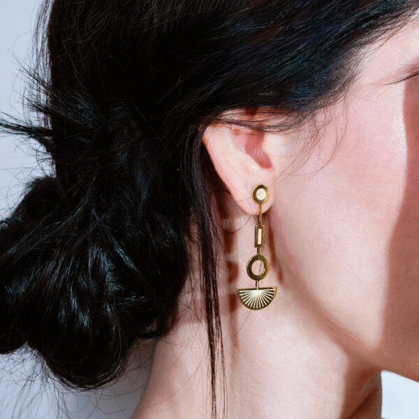 Close-up of a woman's ear wearing a stylish gold dangle earring with geometric shapes.